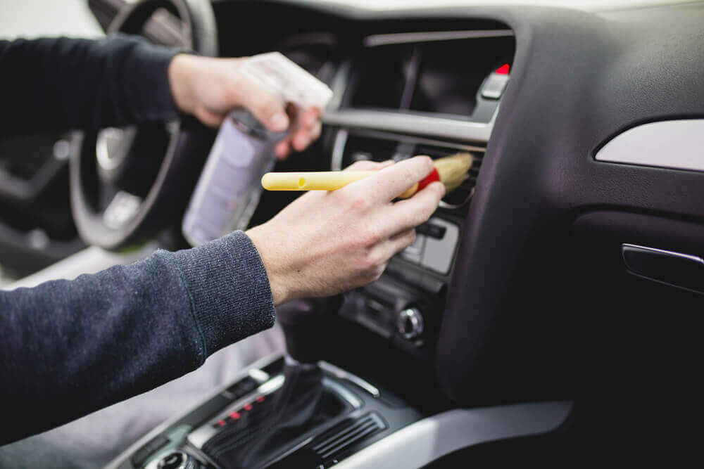 a detailer using a paint brush to clean the inside vents of a car