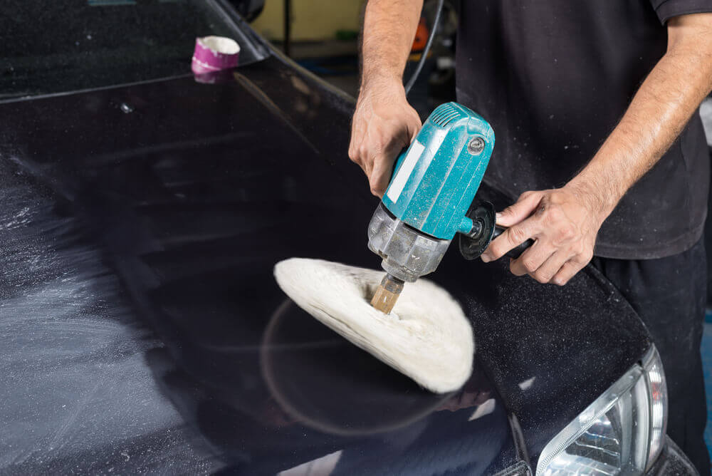 a car detailing worker using a wool polishing machine to clean the bonnet of a black car