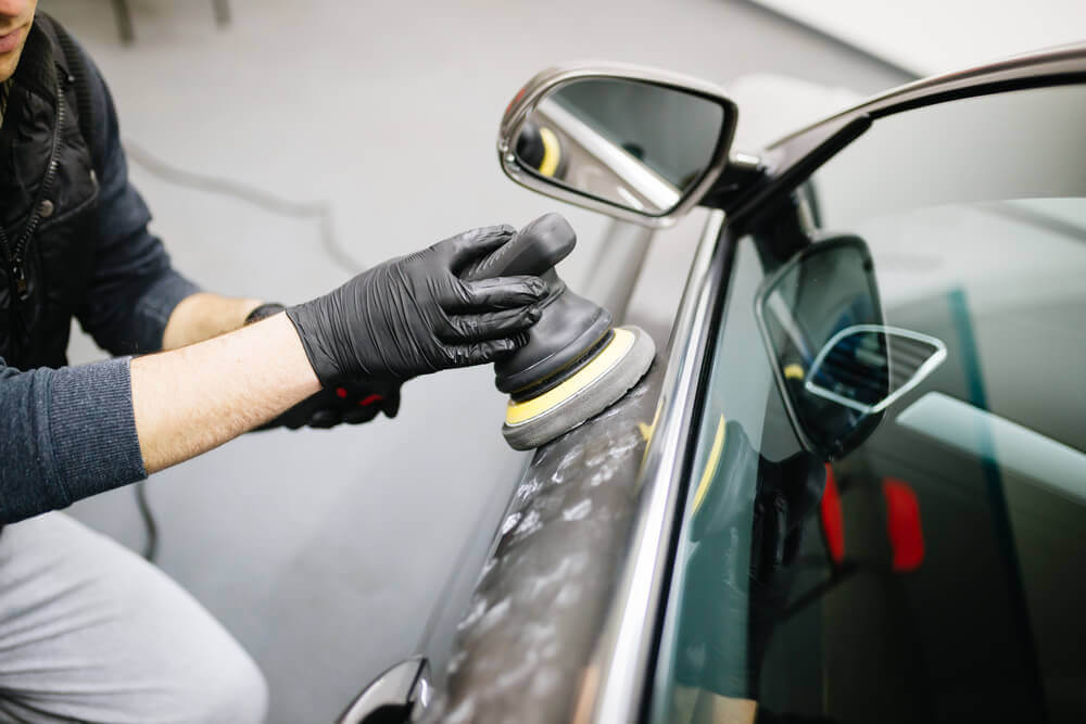 a worker polishing the side of a car with an electric buffer