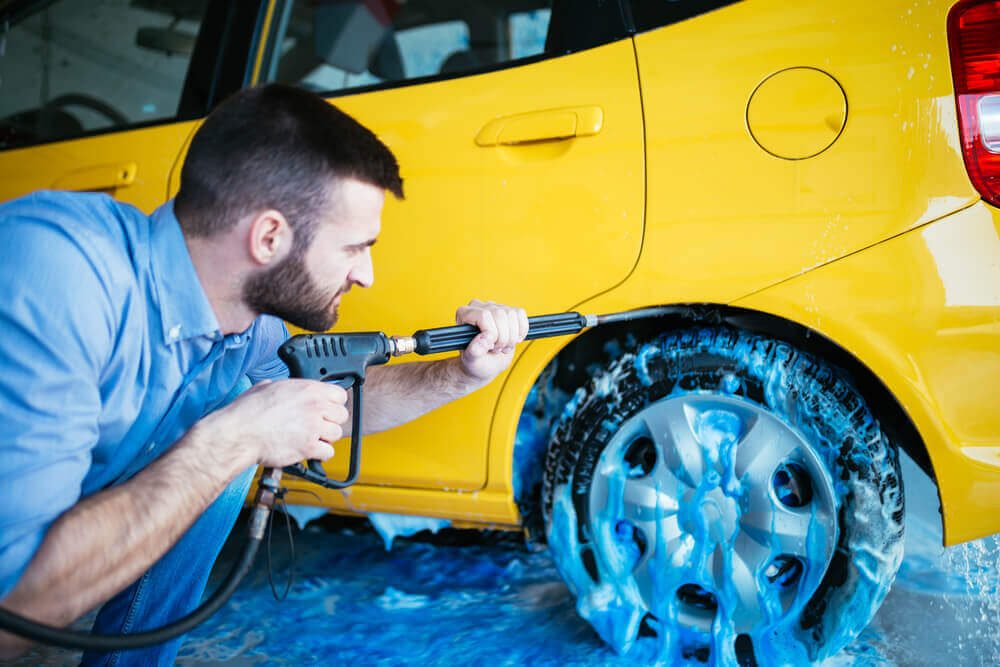 a yellow car getting its rims cleaned with a bright blue foam and high pressure washing gun at car detailing Toowoomba