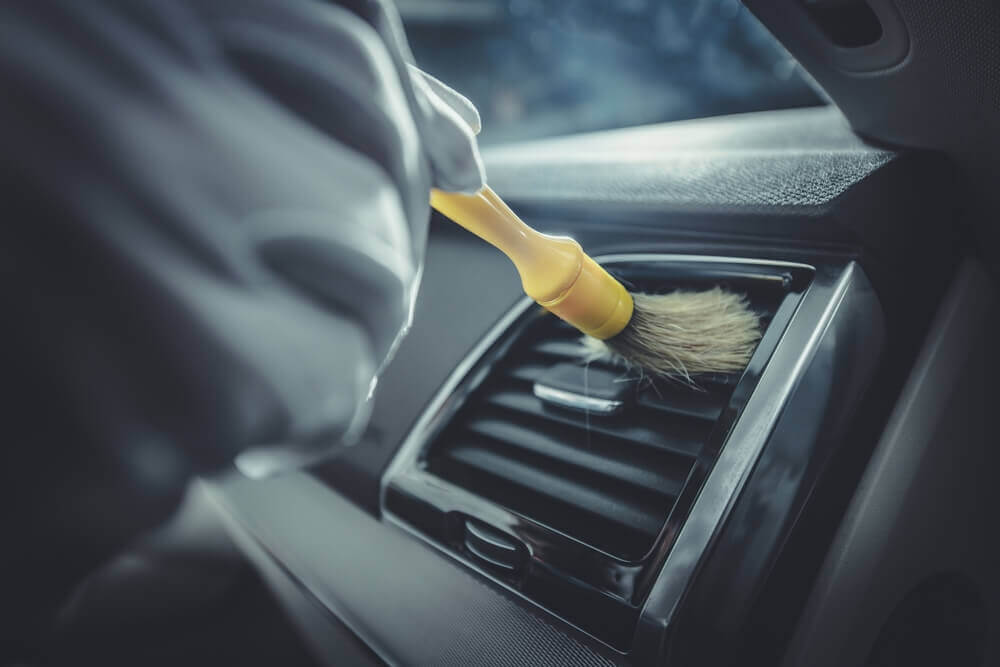 a worker using a paint brush to clean the inside vents of a car