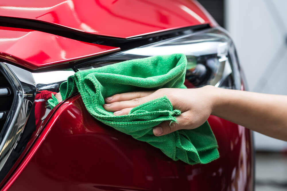 a close up shot of a red car's headlight being wiped over with a green cloth